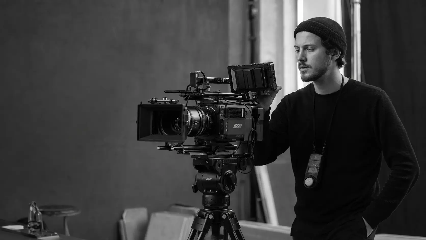 Młody operator filmowy w czapce sprawdzający kadr przy kamerze ARRI ze światłomierzem na szyi